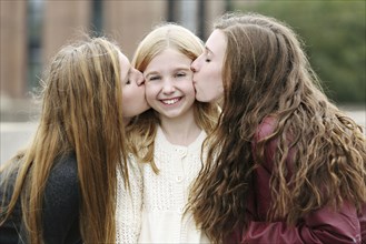Close up of smiling sisters kissing outdoors