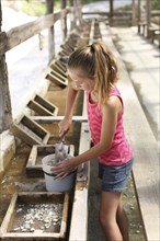 Girl shoveling rocks in bucket in trough