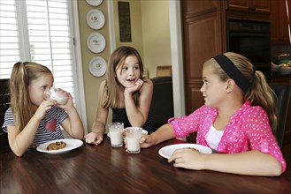 Sisters eating cookies with milk at table