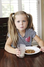 Girl eating cookies with milk mustache at table