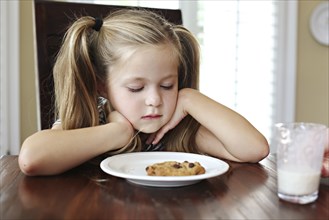Girl staring at cookie with milk at table