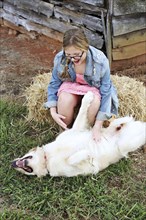 Caucasian girl scratching belly of dog on farm
