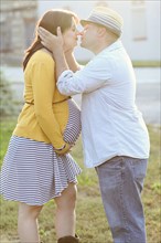 Pregnant couple kissing in sunny field