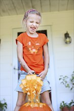 Caucasian girl carving pumpkin on front porch
