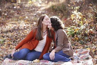 Caucasian lesbian kissing cheek of girlfriend in autumn leaves
