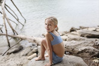 Caucasian girl in bikini sitting by remote lake