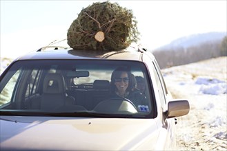 Woman driving Christmas tree home on car roof