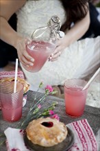 Woman pouring pink lemonade into glasses on wooden table