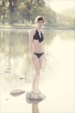 Woman in lingerie standing on rock in still pond