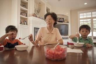 Asian grandmother feeding grandsons at table
