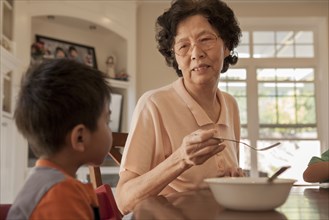 Asian grandmother feeding grandson at table