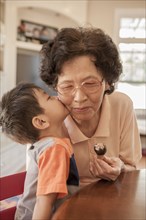 Asian boy kissing grandmother at table