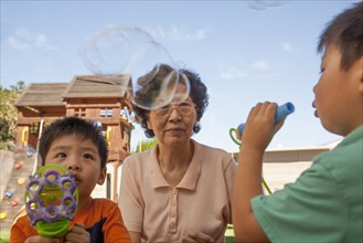 Asian grandmother and grandsons blowing bubbles outdoors