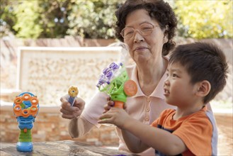 Asian grandmother and grandson blowing bubbles outdoors