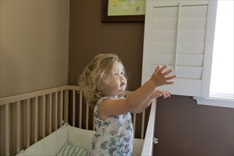 Pouting preschooler girl reaching out of crib