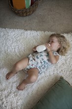 High angle view of preschooler girl drinking bottle on rug