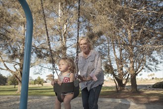 Grandmother pushing granddaughter on swing at playground