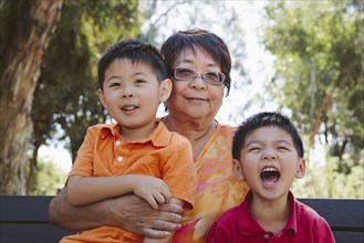 Asian grandmother sitting with grandsons on bench