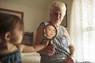 Grandmother holding mirror for granddaughter on bed