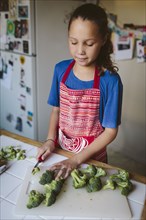 Smiling girl chopping broccoli in kitchen
