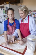 Grandmother and granddaughter rolling dough in kitchen
