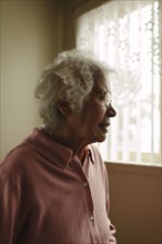 Older mixed race woman standing at window