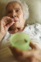 Older mixed race woman taking medication in bed