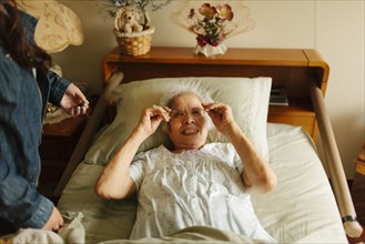 Granddaughter giving grandmother eyeglasses in bed