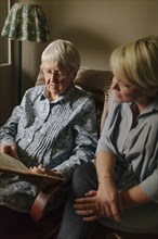Older woman reading to granddaughter in living room