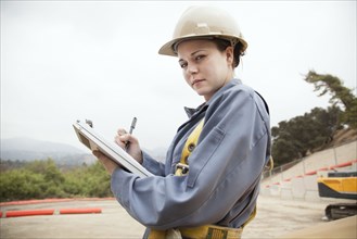Worker writing on clipboard at construction site