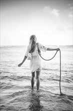 Caucasian woman wading in ocean waves holding rope