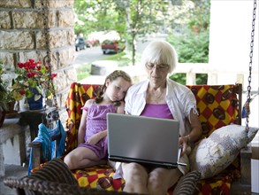 Grandmother and granddaughter using laptop on porch