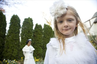 Caucasian girls wearing white dresses walking in garden