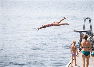 Caucasian girl jumping from diving board into lake