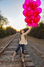 Caucasian teenage girl holding bunch of balloons on train tracks
