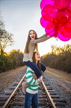 Caucasian teenage girl carrying sister on shoulders with balloons