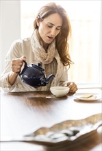 Caucasian woman pouring cup of tea at table