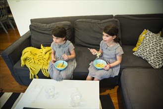 Twin sisters eating on sofa