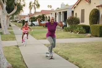 Mother and daughter riding skateboard and bicycle on sidewalk