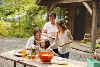 Three generations of Caucasian women cooking outside cabin