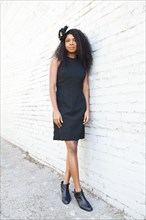 Stylish Black woman leaning on brick wall