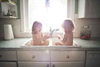 Twin girls bathing in kitchen sink