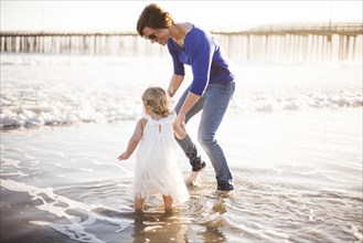 Caucasian mother and daughter walking on beach