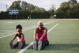 Grandmother and granddaughter stretching on football field