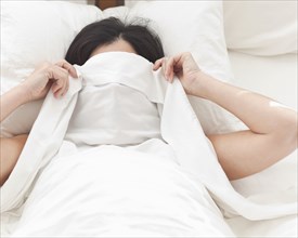 Hispanic woman in bed covering her face