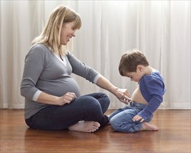 Pregnant Caucasian mother sitting on floor with son