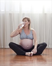 Pregnant Caucasian woman sitting on floor drinking water