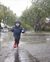 Caucasian boy splashing in rain puddle