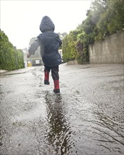 Caucasian boy walking in rain puddle