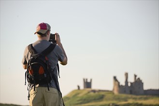 Caucasian tourist photographing Dunstanburgh castle